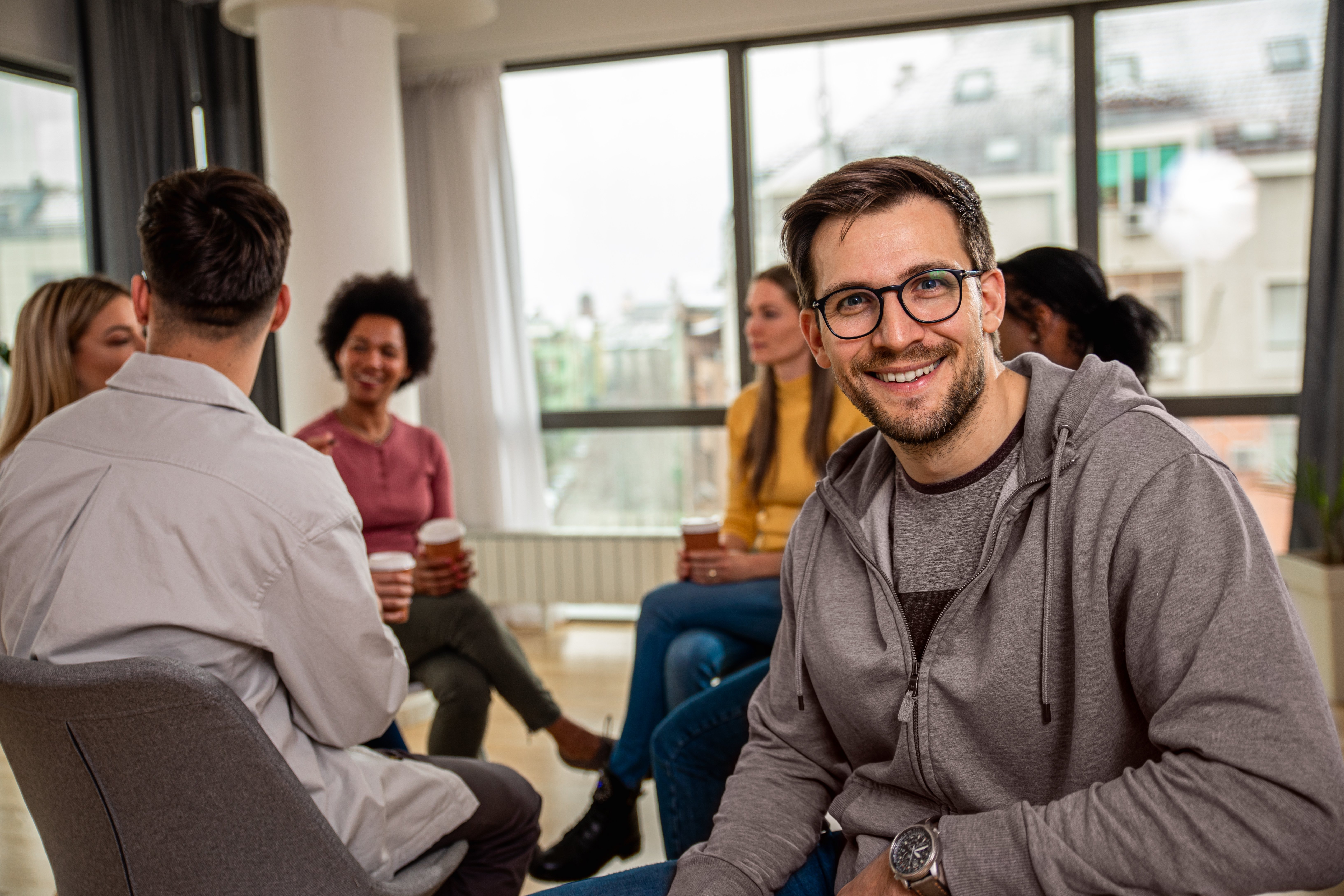 Portrait of a man with diverse group of people sitting in circle in group therapy session.